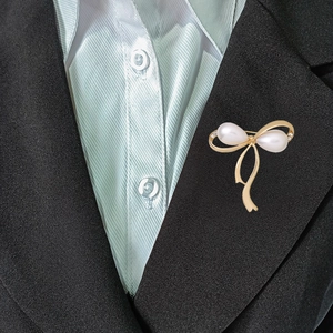 Elegante broche de lazo dorado con perlas blancas y circonitas sobre solapa negra