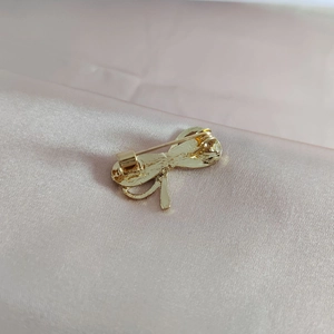 Elegant gold bow brooch pin with secure needle clasp closure on pink satin fabric background