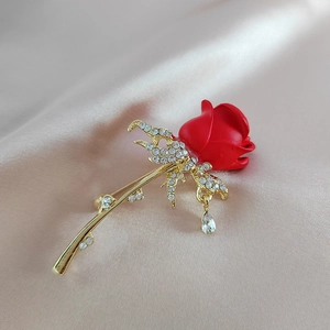 Détail broche rose rouge avec tige dorée, feuilles en diamant et pendentif en goutte