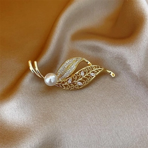 Elegant gold leaf brooch with crystals and pearl on champagne silk background
