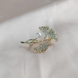 Makroansicht der goldenen Ginkgo-Brosche mit Kristallen und Perle auf champagnerfarbener Seide