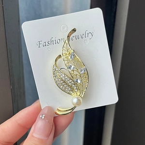 Detail of leaf-shaped brooch with sparkling rhinestones and a white pearl on a card