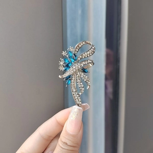 Macro detail of a bow-shaped brooch featuring blue marquise gems and white rhinestones