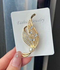 Close-up of golden leaf brooch with sparkling crystals and a white imitation pearl
