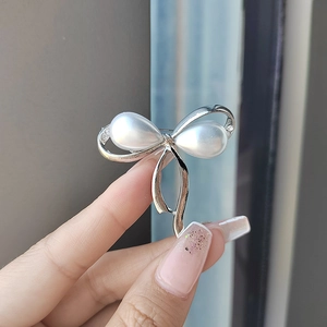 Elegante broche de lazo plateado con perlas blancas de gota y detalles de strass