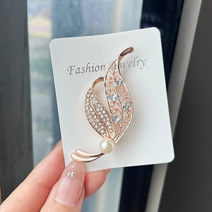 Close-up of rose gold leaf brooch featuring white rhinestones and a white faux pearl detail
