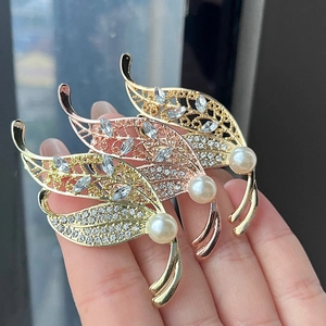 Detailed view of hand-held leaf brooches featuring sparkling crystals and white pearls