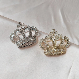 Broches couronne étincelantes en or et argent avec détail croix sur fond de satin rose