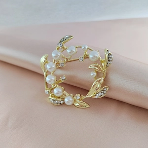 Elegant gold flower wreath brooch with pearls and crystals on soft silk fabric background