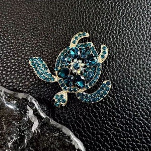 Exquisite vergoldete Schildkröten-Brosche mit blauen Kristallen auf schwarzem Lederhintergrund