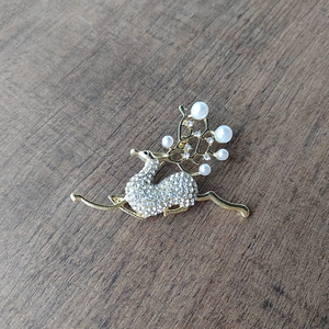 Close-up of golden deer brooch featuring white rhinestones and faux pearls on antlers