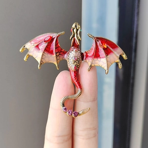 Elegant gold-plated dragon brooch with red enamel wings and pink crystals held in fingers