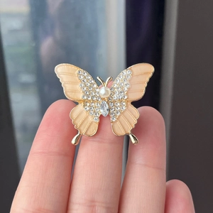Golden butterfly brooch with pearls and rhinestones shown held in hand closeup