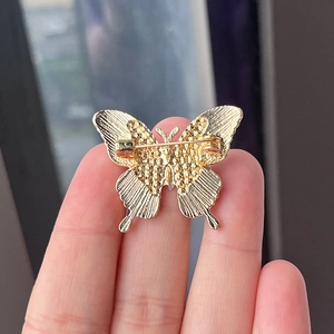 Back view of a gold butterfly brooch showing the safety pin clasp and metal texture