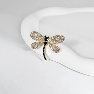 Close-up of golden dragonfly brooch featuring white rhinestones and deep green gemstones
