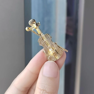 Elegant gold violin brooch with brushed metal finish held by hand to show its petite size