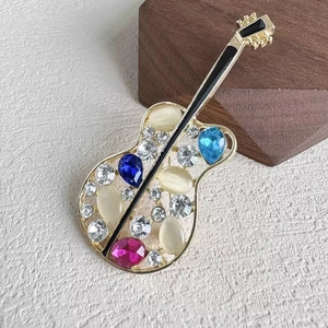 Broche guitare dorée avec pierres d'opale et cristaux colorés sur fond blanc