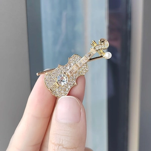 Elegant gold violin brooch with sparkling rhinestones and a white pearl on hand