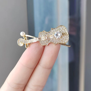 Elegant gold-tone violin brooch with sparkling rhinestones and pearl detail held in hand