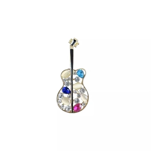 Broche guitare dorée avec opale et strass scintillants sur fond blanc immaculé