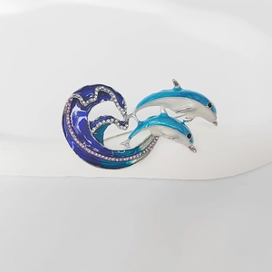 Dettaglio della spilla delfino con smalto blu e strass rosa scintillanti sulle onde