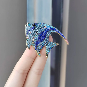 Close-up of hand holding a tropical fish brooch with blue and purple rhinestones