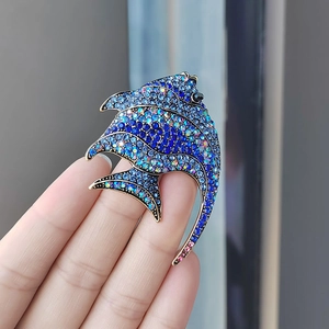 Detail of vintage angel fish brooch with blue crystals held in hand for size context