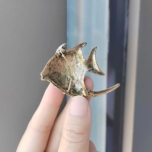 Hand holding tropical fish brooch in antique gold with crystal details and secure pin back