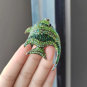 Detailed view of fish brooch with green crystals and gold base on a hand