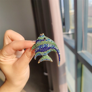 Detailed view of fish brooch with blue and green crystals held in hand under natural light