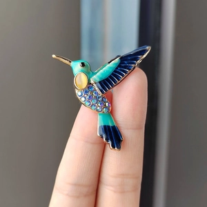 Makro-Detail einer Kolibri-Brosche mit blauen Strasssteinen, zwischen Fingern gehalten