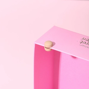 Gros plan d'une pince magnétique ronde beige pour hijab et écharpe sur boîte rose