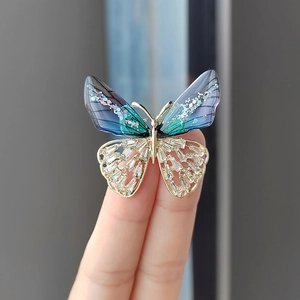 Vista de un broche de mariposa dorado con alas degradadas azul-violeta y circonitas