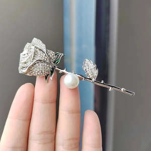 Detail of rose brooch with white rhinestones, green enamel leaf, and white pearl on silver stem