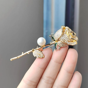 Close-up of rose brooch featuring white crystals, round pearl, and green enamel leaves