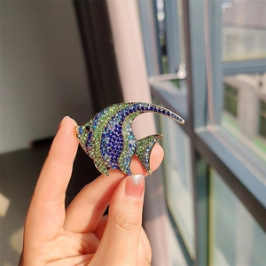Detailed view of hand-held tropical fish brooch with vibrant blue and green crystals