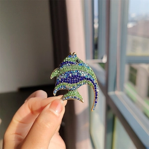 Close-up of a hand holding a gold tropical fish brooch with blue and green rhinestones