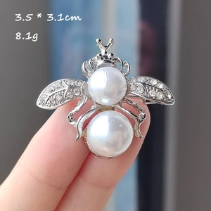 Détail d'une broche abeille argentée avec perles blanches et strass brillants 3,5x3,1cm