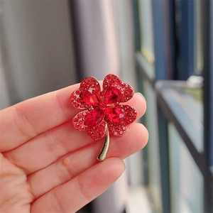 Close-up of hand holding a gold four-leaf clover brooch with red crystal rhinestones