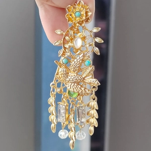 Detail of vintage gold hummingbird brooch with faux pearls, emerald stones and tassel pendant