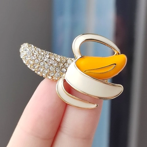 Charming banana-shaped brooch pin with rhinestones and colorful enamel held by fingers