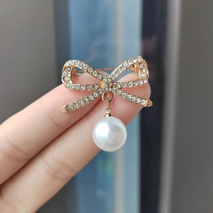 Eleganter Strass-Schleifenbrosche mit weißem Perlenanhänger, handgehalten präsentiert