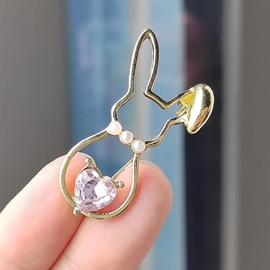 Detailed view of a gold rabbit brooch with three white pearls and a pink heart crystal