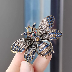 Detail of vintage gold bee brooch with blue and amber rhinestones held in hand
