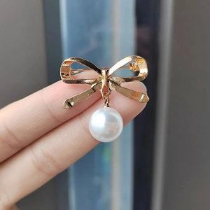 Eleganter goldener Schleifen-Brosche mit weißem Perlenanhänger in der Hand