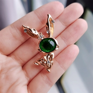 Detailed macro of a gold rabbit brooch with a large green gemstone and zircon accents