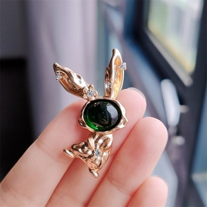 Close-up of golden bunny brooch featuring a green cabochon gem and small white rhinestones