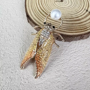 Close-up of golden cicada brooch featuring gradient enamel wings and a large white pearl