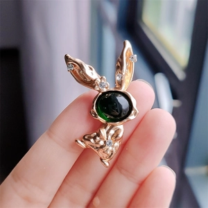 Close-up of golden bunny brooch with green gemstone and crystals held by a hand