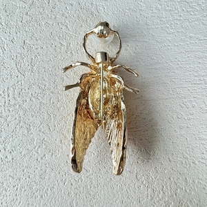 Detailed back view of gold insect cicada brooch with safety pin and white faux pearl